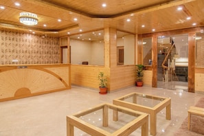 A reception area with a wooden reception desk, a reception sign, a staircase, and potted plants. - Indrasan Manali (Manali)