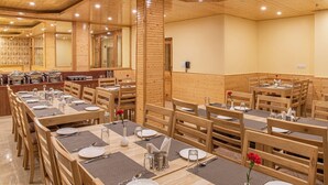 Un restaurante con mesas y sillas de madera, dispuesto en un amplio salón comedor con techos altos y un ambiente cálido.