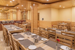 A restaurant with wooden tables and chairs, arranged in a spacious dining area with high ceilings and a warm ambiance. - Indrasan Manali (Manali)