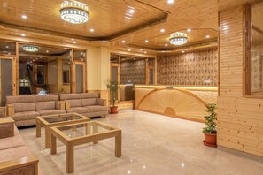 A hotel lobby with a reception desk, sofas, and a coffee table. - Indrasan Manali (Manali)
