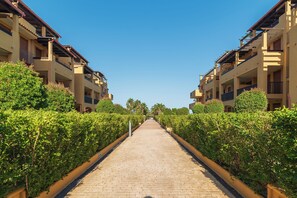 A pathway flanked by buildings with balconies, leading to a clear blue sky.