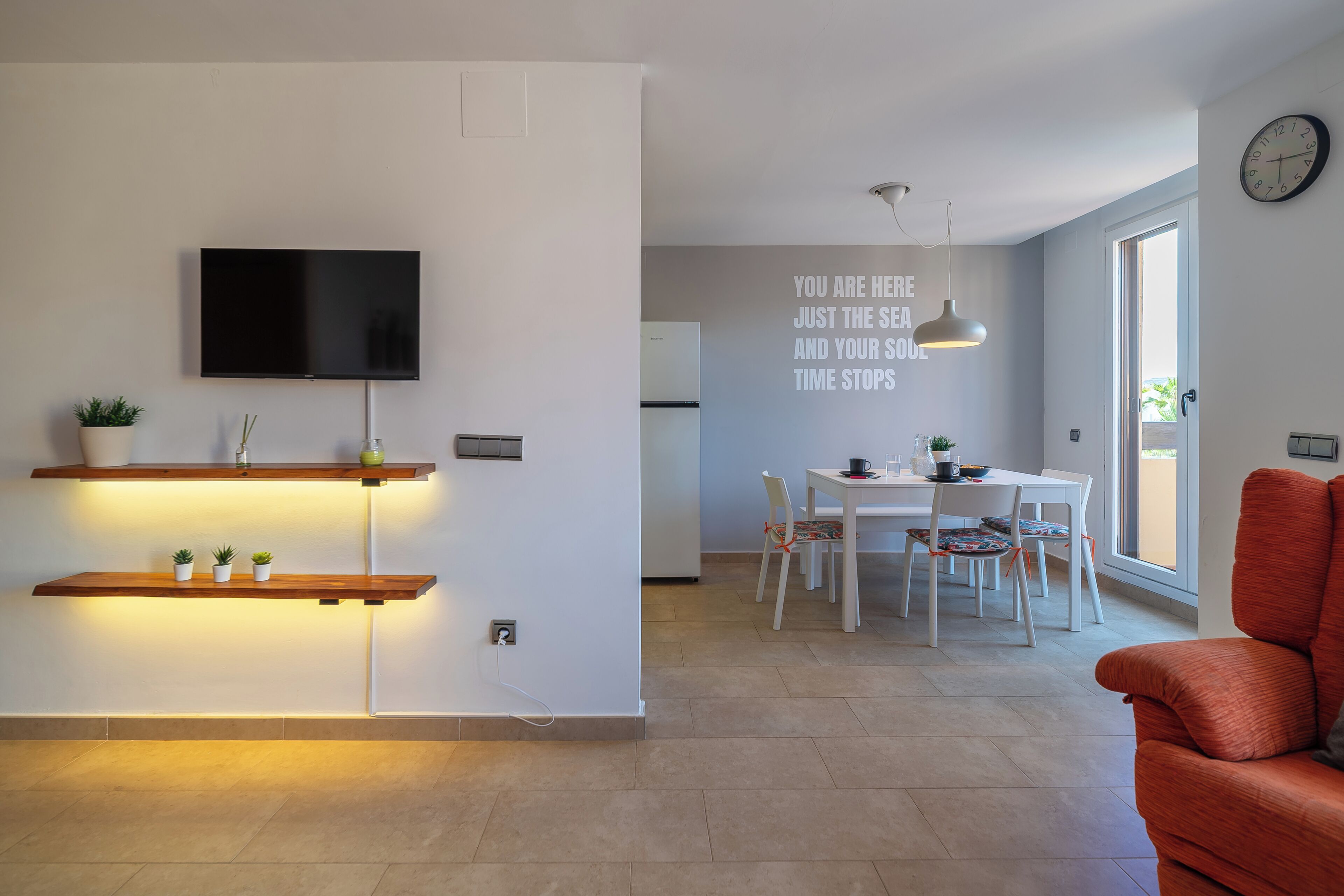 Ein modernes Wohnzimmer mit Flachbildfernseher, Holzregalen und einem Essbereich mit Tisch und Stühlen.