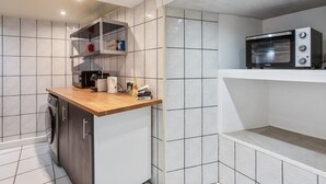 Une cuisine compacte dotée d’un lave-vaisselle encastré, d’une machine à café et d’un four à micro-ondes, le tout installé sur un mur recouvert de carreaux blancs.