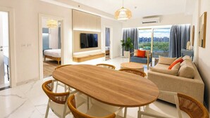 A modern living room with a wooden dining table, wicker chairs, a sofa, and a television mounted on the wall.