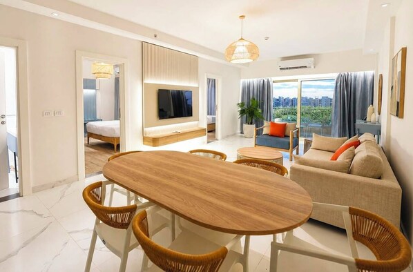 A modern living room with a wooden dining table, wicker chairs, a sofa, and a television mounted on the wall. - MISK Marina Valley (Marsa Matrouh Governorate)