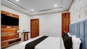 A modern hotel room with a wooden headboard, a flat-screen TV, a small table with a kettle, and a bed with white and black bedding. - Super Collection O AIIMS Bhubaneshwar (Bhubaneshwar)