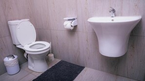 Un baño moderno con inodoro, lavamanos empotrado y un cubo de basura.