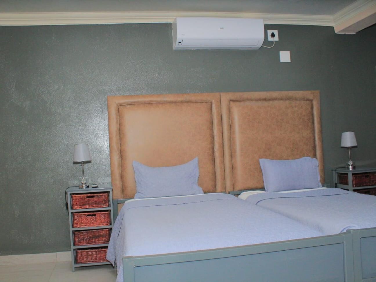 A bedroom with a bed, two nightstands, a wall-mounted air conditioner, and a wall with a textured finish.