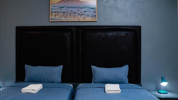 Una habitación con dos camas, un cuadro de una playa y una mesita de noche con una lámpara.