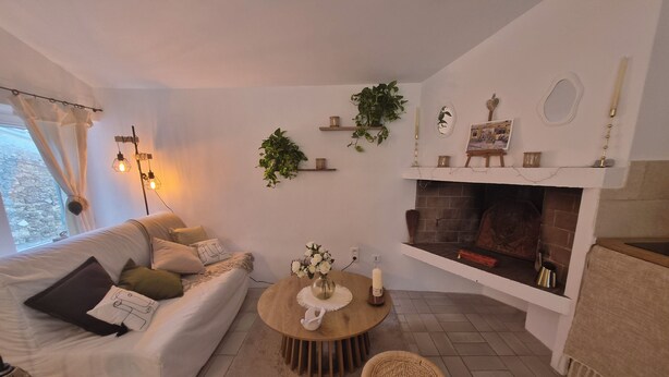 Een woonkamer met een bank, een rond bijzettafeltje, een open haard en een raam met gordijnen.