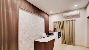 A reception desk with a white counter, a wooden panel wall, a marble wall, beige curtains, and an air conditioning unit on the wall. - Collection O Ravi Talkies Bhubaneswar (Bhubaneshwar)