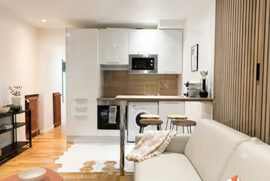 Eine moderne Küche mit weißen Schränken, einer Mikrowelle und einem eingebauten Backofen. Ein Sitzbereich mit einer Couch und einem kleinen Tisch ist ebenfalls vorhanden.