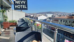 Mesa de comedor en la azotea con diversos alimentos, como pan, huevos y verduras, con vistas a un paisaje urbano.
