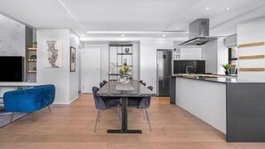 Et moderne køkken med en central ø, et spiseområde med et mørkt bord og stole, og en blå sofa.