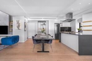 Eine moderne Küche mit einer zentralen Kochinsel, einem Essbereich mit dunklem Tisch und Stühlen sowie einem blauen Sofa.