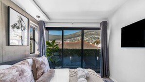 Et moderne soveværelse med en stor seng, et fladskærms-tv og en balkon med udsigt over byen.