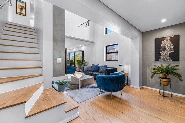 Ein modernes Interieur mit Treppe, einem Wohnbereich mit Sofa und Sesseln sowie einem großen Fenster.