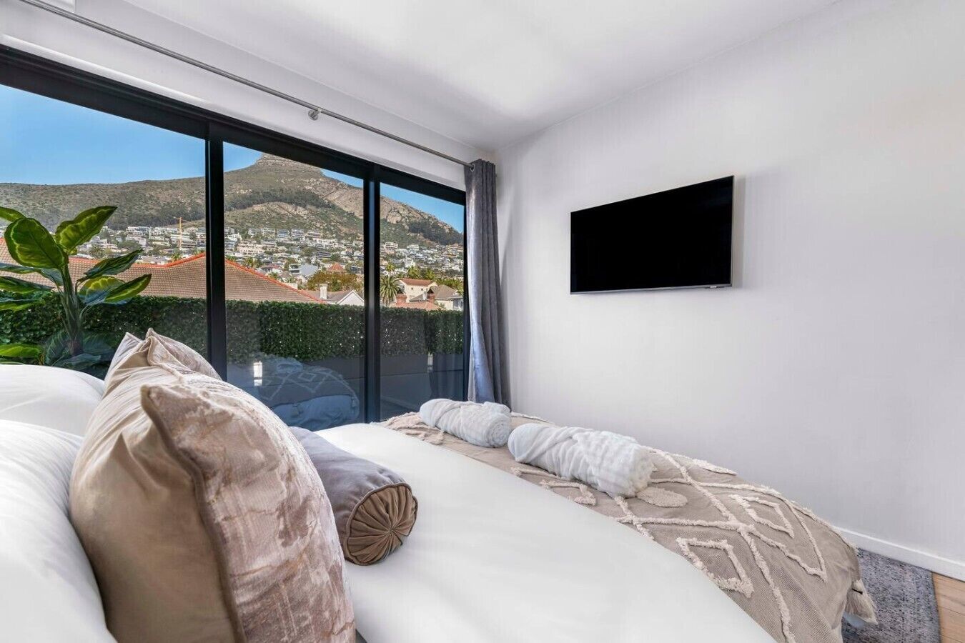 A modern bedroom with a large bed, a flat-screen TV, and a view of a cityscape through large windows.