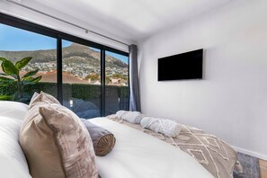 Ein modernes Schlafzimmer mit einem großen Bett, einem Flachbildfernseher und Blick auf eine Stadtlandschaft durch große Fenster.