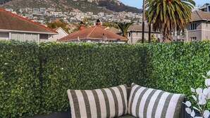 En balkon med et grønt polstret siddeområde, et lille bord og udsigt til et bjerg og bybillede.