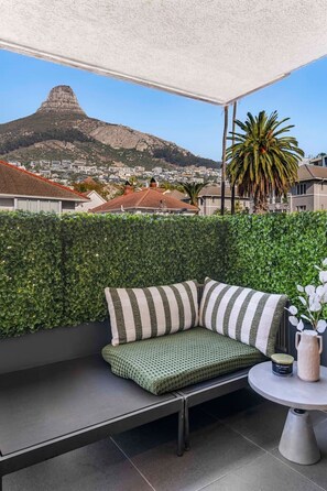 Ein Balkon mit grünen Sitzkissen, einem kleinen Tisch und Blick auf Berge sowie Stadtlandschaft.