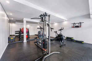 Ein Fitnessraum mit Trainingsgeräten, einer Spiegelwand und einer Tür zu einem weiteren Raum.