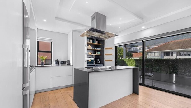 A modern kitchen with a central island, built-in shelves, and a large window overlooking a residential area.