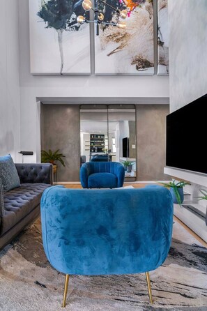 Un salon moderne avec un fauteuil en velours bleu, un canapé gris et un téléviseur à écran plat.