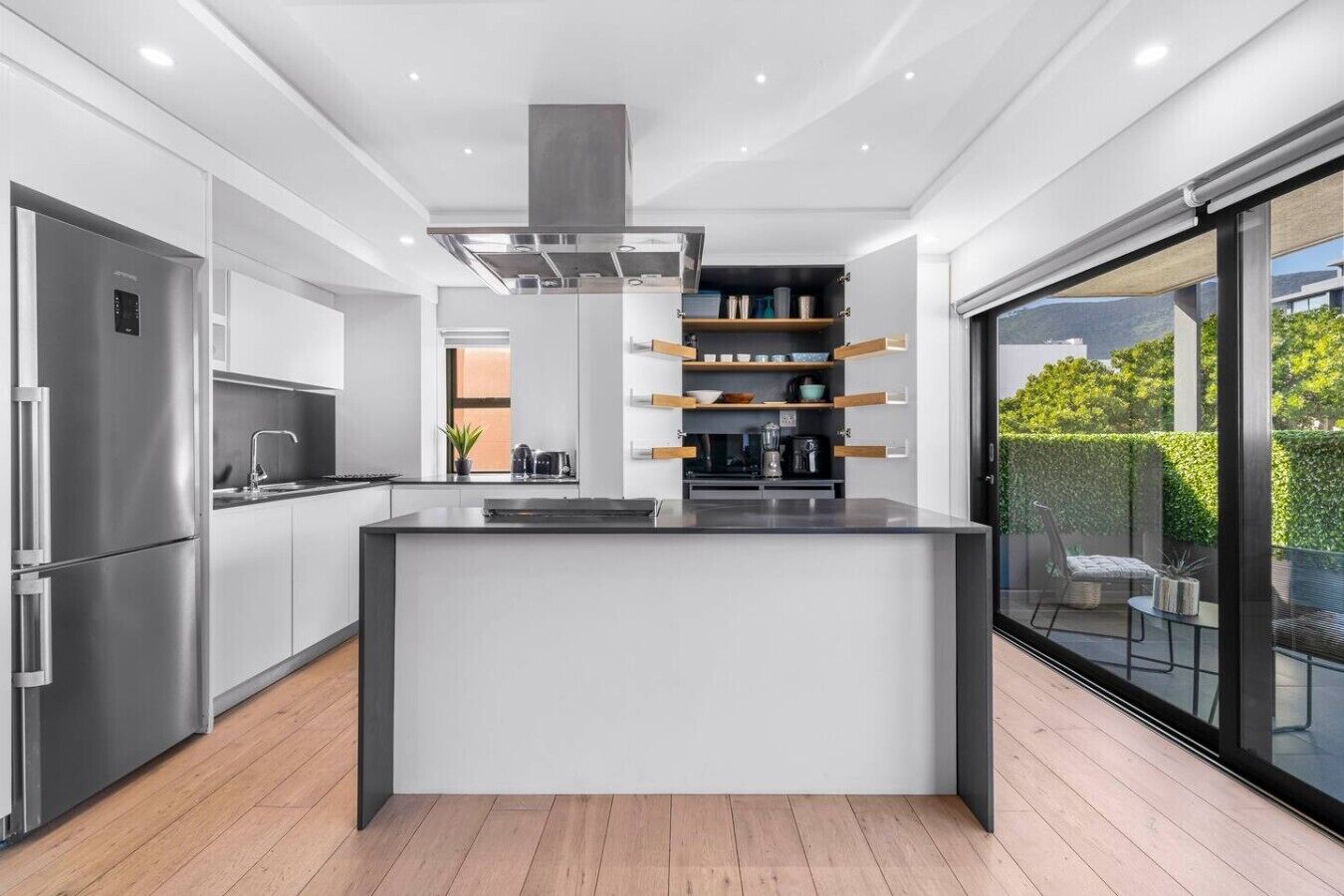 A modern kitchen with a central island, built-in appliances, and a sliding glass door to an outdoor area.