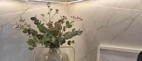 A kitchen with a marble countertop, a stainless steel sink, a vase with green foliage, and three striped containers.