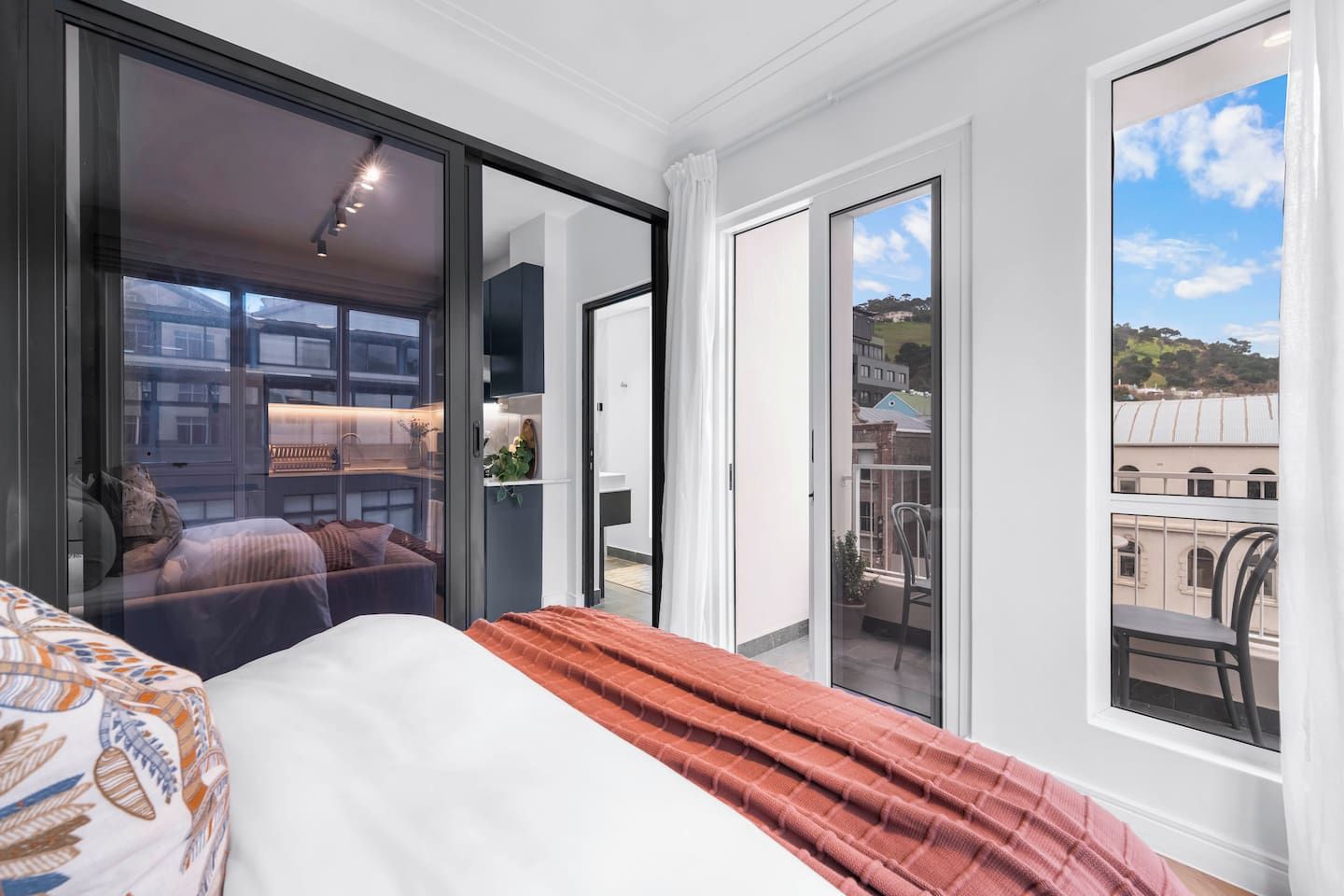 A modern bedroom with a bed, a large window, and a sliding door leading to a balcony.
