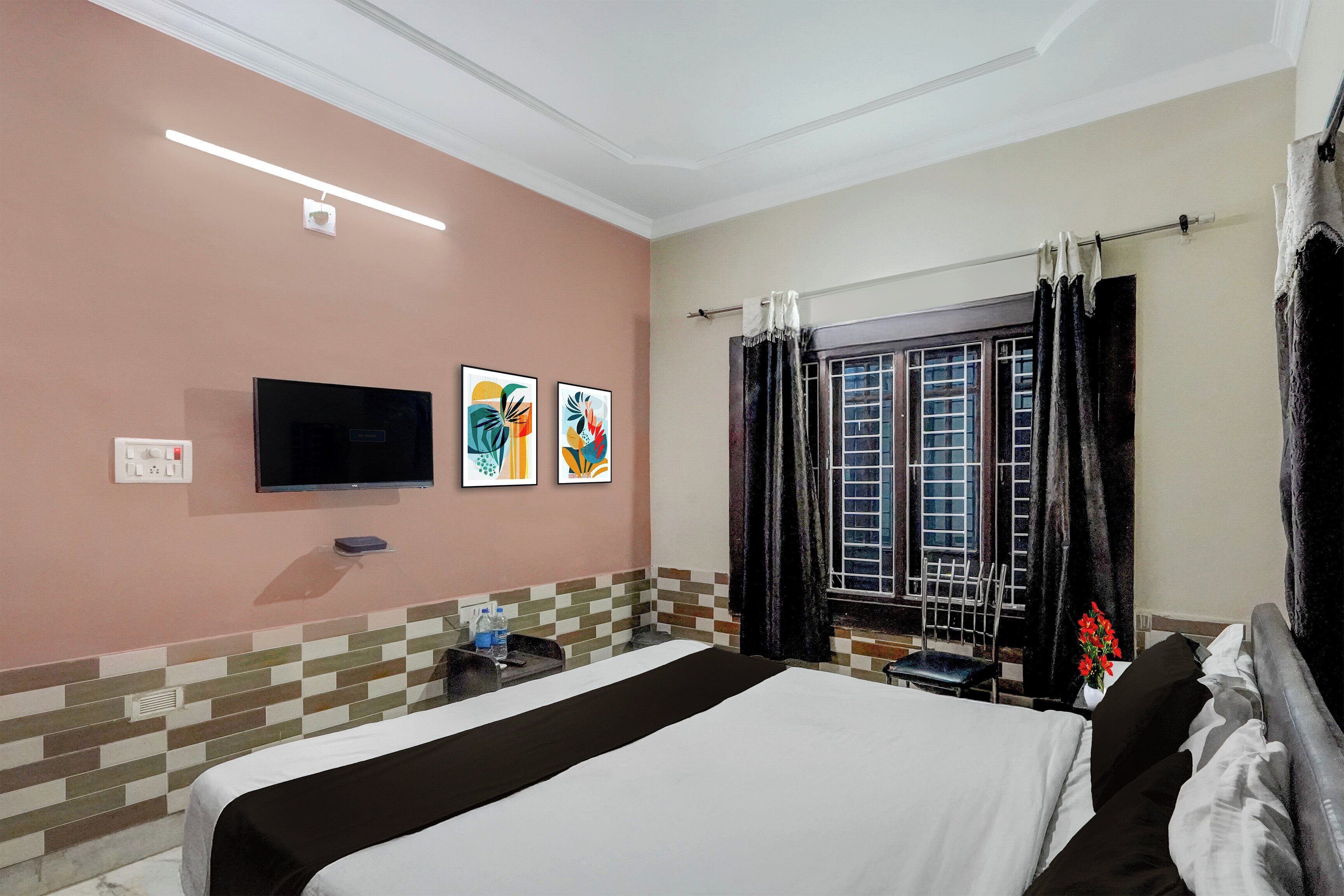 Habitación de hotel con cama, televisor de pantalla plana, obras de arte en la pared, ventana con cortinas y un salpicadero de azulejos.