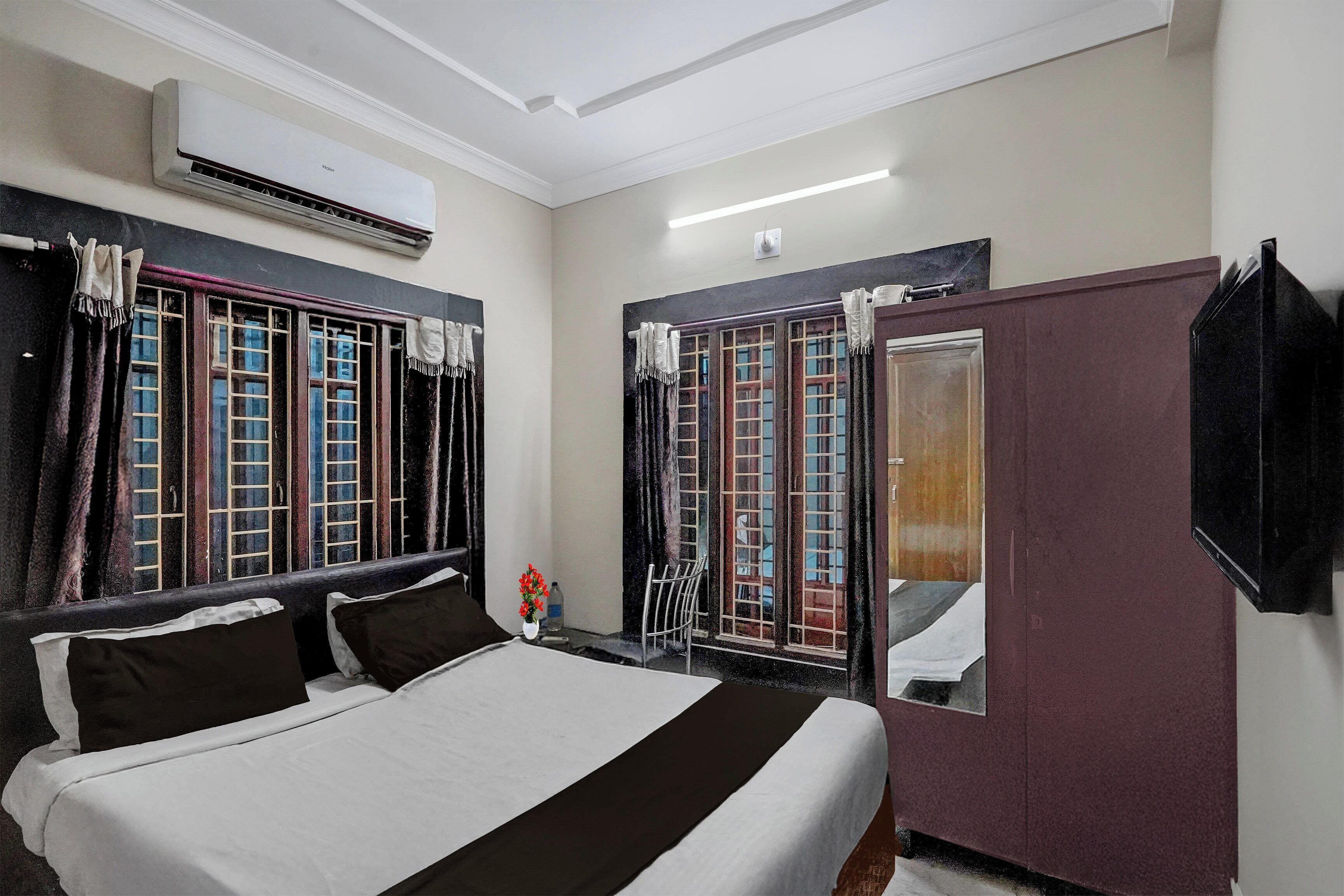 A hotel room with a bed, a wardrobe, a mirror, and a window with curtains.