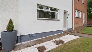 Een twee verdiepingen tellend huis met een witte gevel, een kleine voortuin met witte kiezelstenen en een hoge, smalle plantenbak.
