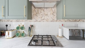 Een keuken met een gasfornuis, witte kastjes en een marmeren achterwand.