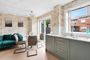 Eine moderne Küche mit Marmor-Spritzschutz, ein Essbereich mit einem grünen Sofa und Blick auf die Nachbarschaft.