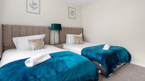 Een hotelkamer met twee bedden, een nachtkastje met een lamp, en twee ingelijste plantenfoto's aan de muur.