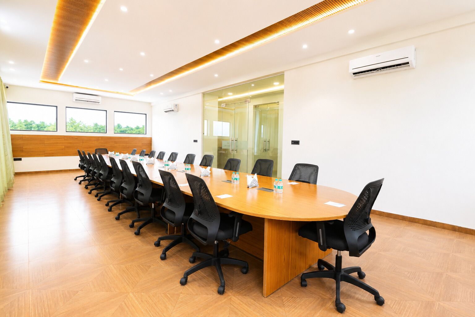 A conference room with a long table, black chairs, and a wooden floor.