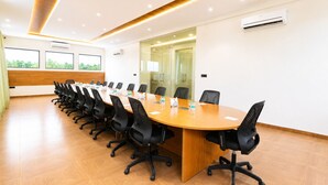 Un salón de conferencias con una larga mesa, sillas negras y piso de madera.