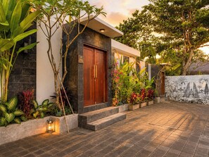 A modern house with a wooden door, a stone wall, and a garden with various plants. - 2 Bedroom Pavilion Pool Villa Canggu (Bali)