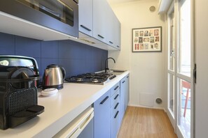 Une cuisine moderne équipée d’une cuisinière à gaz, d’une bouilloire et d’une machine à café. Un tableau encadré représentant des couvertures de vieux magazines de bandes dessinées est accroché au mur.