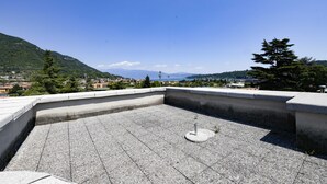 En tagterrasse med beton gulv, en metalstolpe og udsigt til en by og fjerne bjerge.