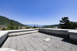 A rooftop terrace with a concrete floor, a metal pole, and a view of a town and mountains in the distance. - MGH - Salò Urban Retreat (Salò)