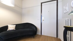 Et værelse med en sort sofa, en hvid dør, en radiator og et lille bord med en lampe.