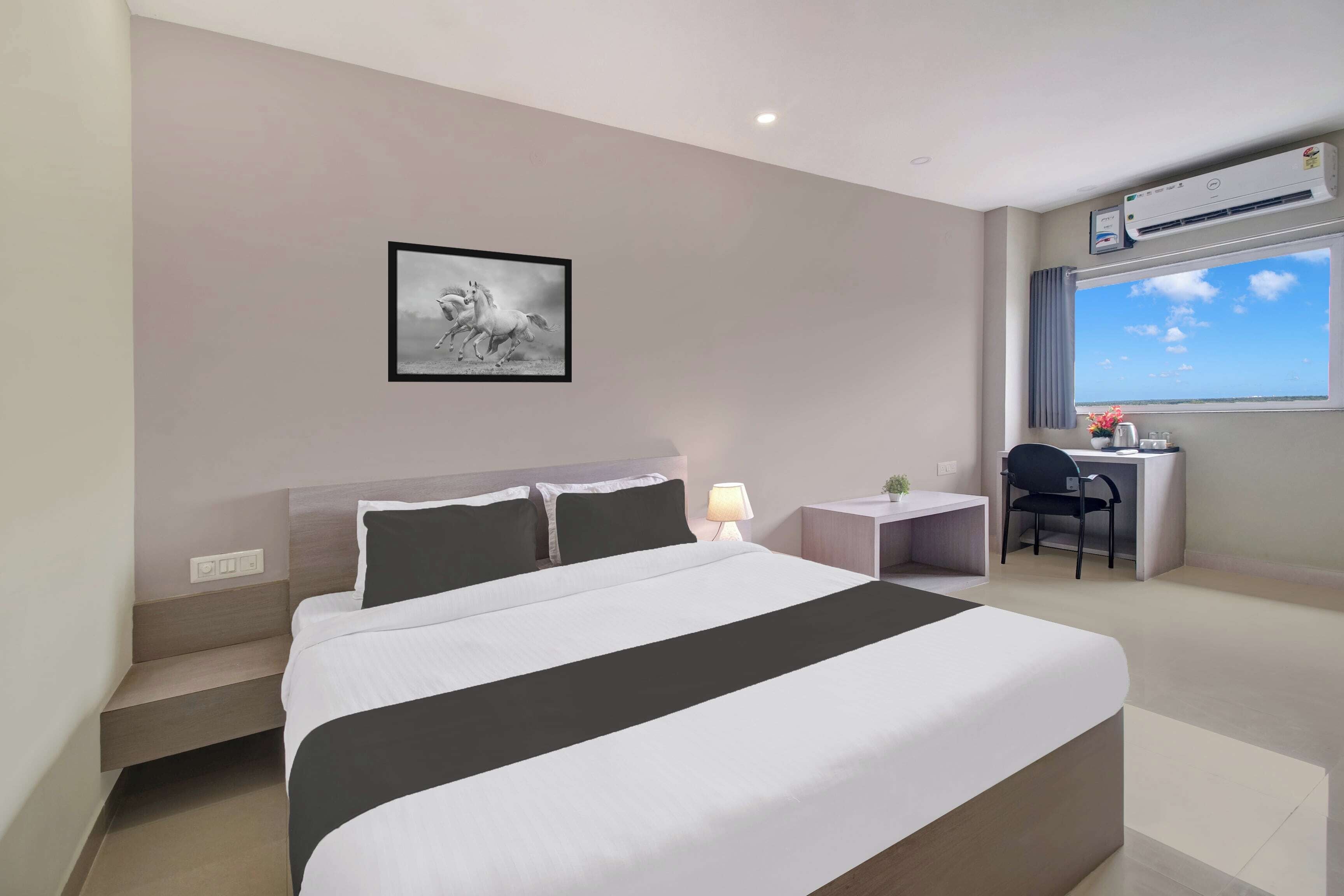 Habitación de hotel con cama, escritorio, silla, ventana con vistas y equipo de aire acondicionado.