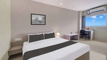 Habitación de hotel con cama, escritorio, silla, ventana con vistas y equipo de aire acondicionado.