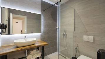 Un baño moderno con ducha envuelta en vidrio, tocador de madera con lavamanos blanco y un espejo grande.