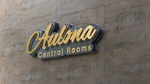 Letrero que dice 'Aurona Central Rooms' sobre una pared con textura y dos macetas con plantas debajo.