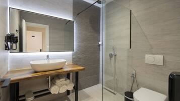 Un baño moderno con un espejo grande, un tocador de madera, un lavabo blanco, cabina de ducha de vidrio y un inodoro.
