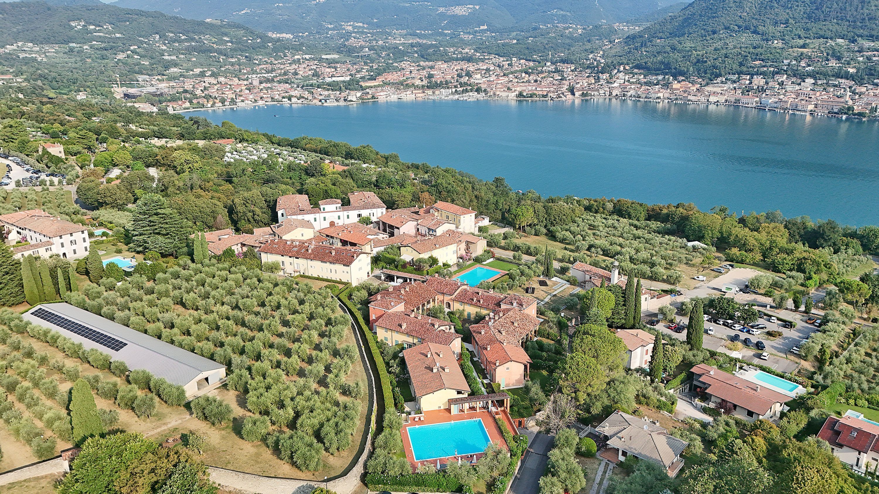 An aerial view of a coastal residential area with houses, a large body of water, and a hilly landscape in the background.